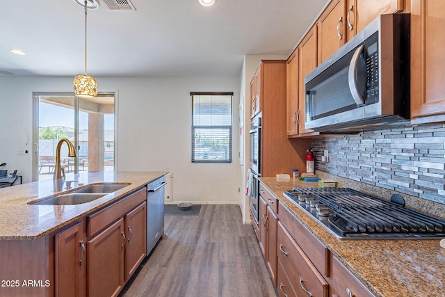 kitchen featuring appliances with stainless steel finishes, a sink, brown cabinets, backsplash, and recessed lighting