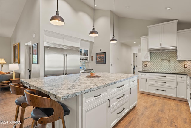 kitchen featuring built in refrigerator, backsplash, white cabinets, and pendant lighting