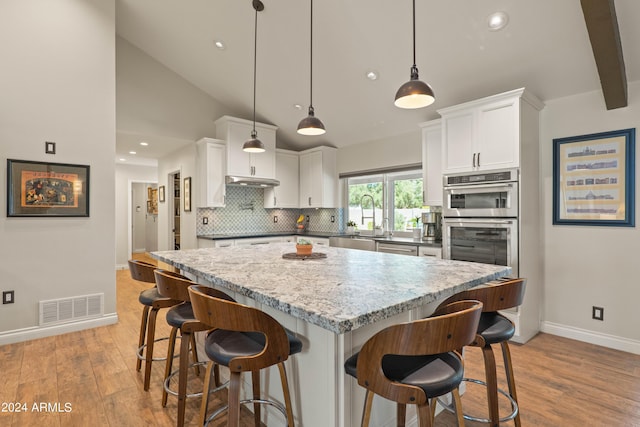 kitchen featuring a kitchen bar, white cabinetry, hanging light fixtures, sink, and a kitchen island