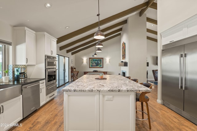 kitchen with white cabinets, a kitchen island, decorative light fixtures, stainless steel appliances, and vaulted ceiling with beams