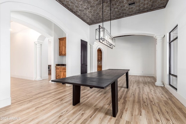 dining area featuring ornate columns, a towering ceiling, light hardwood / wood-style flooring, and an inviting chandelier