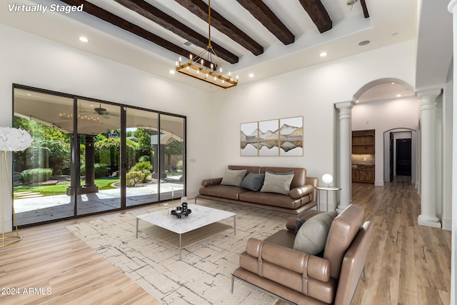 living room with light hardwood / wood-style floors, an inviting chandelier, beamed ceiling, and a towering ceiling