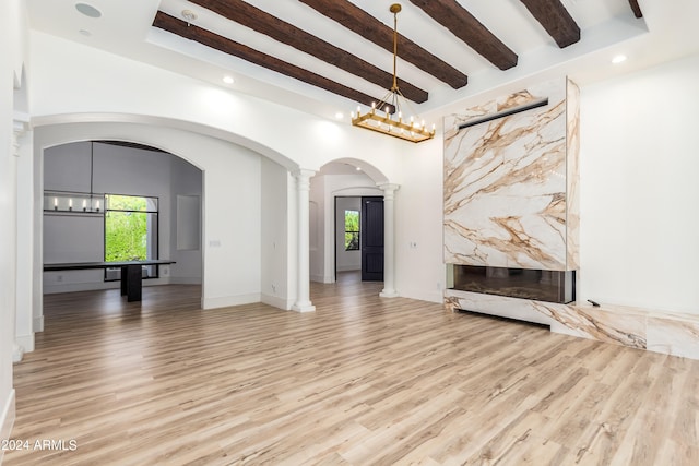 unfurnished living room with light hardwood / wood-style floors, an inviting chandelier, beam ceiling, and ornate columns