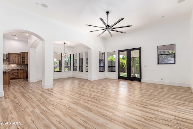 unfurnished living room with light hardwood / wood-style flooring, french doors, and ceiling fan with notable chandelier