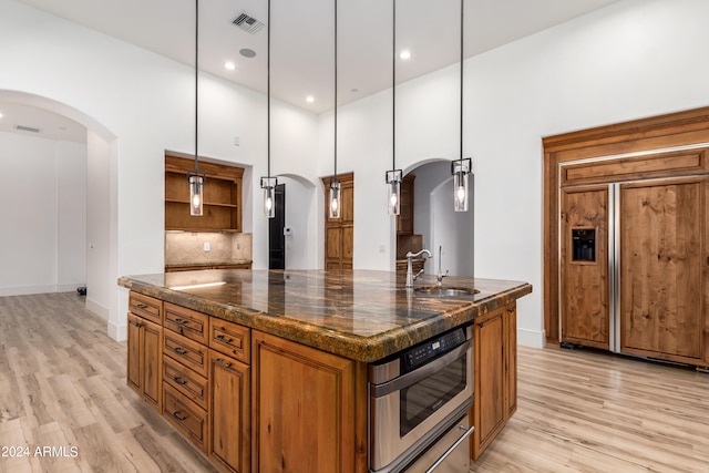 kitchen with a center island with sink, hanging light fixtures, a high ceiling, light hardwood / wood-style floors, and sink