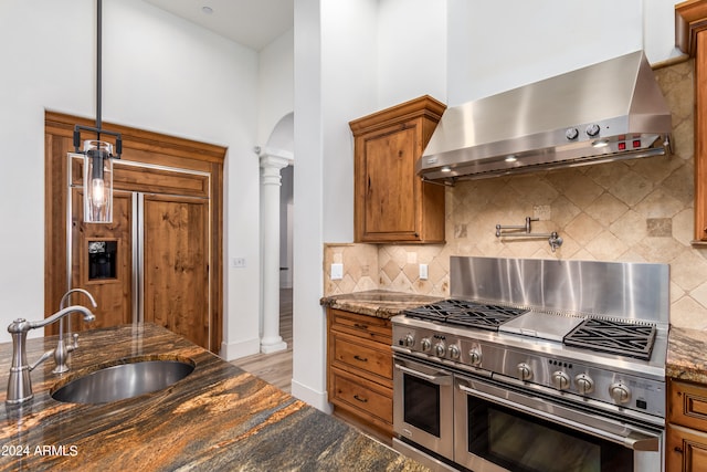 kitchen featuring ornate columns, wall chimney exhaust hood, dark stone counters, and double oven range