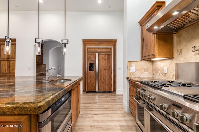 kitchen featuring wall chimney range hood, high quality appliances, sink, decorative light fixtures, and light hardwood / wood-style floors