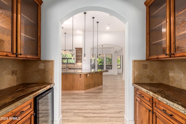 kitchen featuring decorative light fixtures, dark stone counters, wine cooler, decorative backsplash, and light hardwood / wood-style flooring