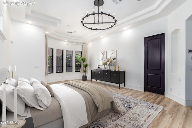 bedroom featuring light hardwood / wood-style flooring, a tray ceiling, and an inviting chandelier