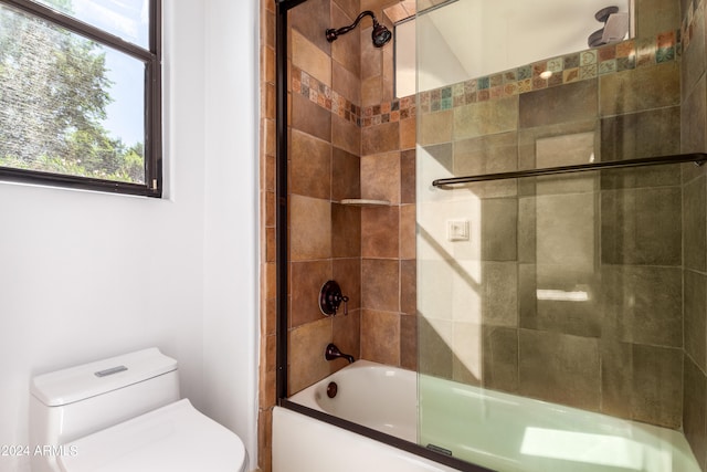 bathroom featuring toilet, a healthy amount of sunlight, and bath / shower combo with glass door