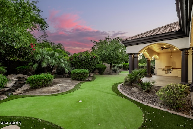 yard at dusk with a patio area, an outdoor kitchen, and ceiling fan