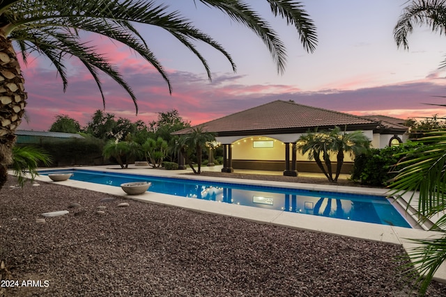 pool at dusk with a patio and a gazebo