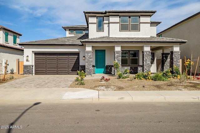 prairie-style house featuring stone siding, decorative driveway, covered porch, an attached garage, and stucco siding