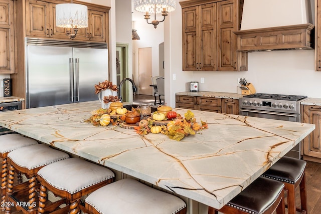 kitchen with an island with sink, hanging light fixtures, premium appliances, dark wood-type flooring, and custom range hood