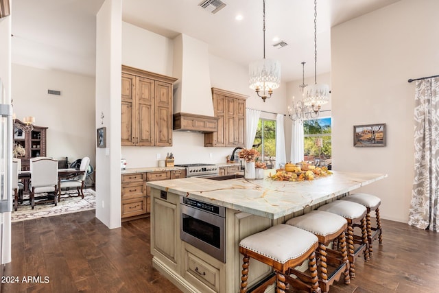 kitchen with an island with sink, dark wood-type flooring, a notable chandelier, custom exhaust hood, and a kitchen breakfast bar