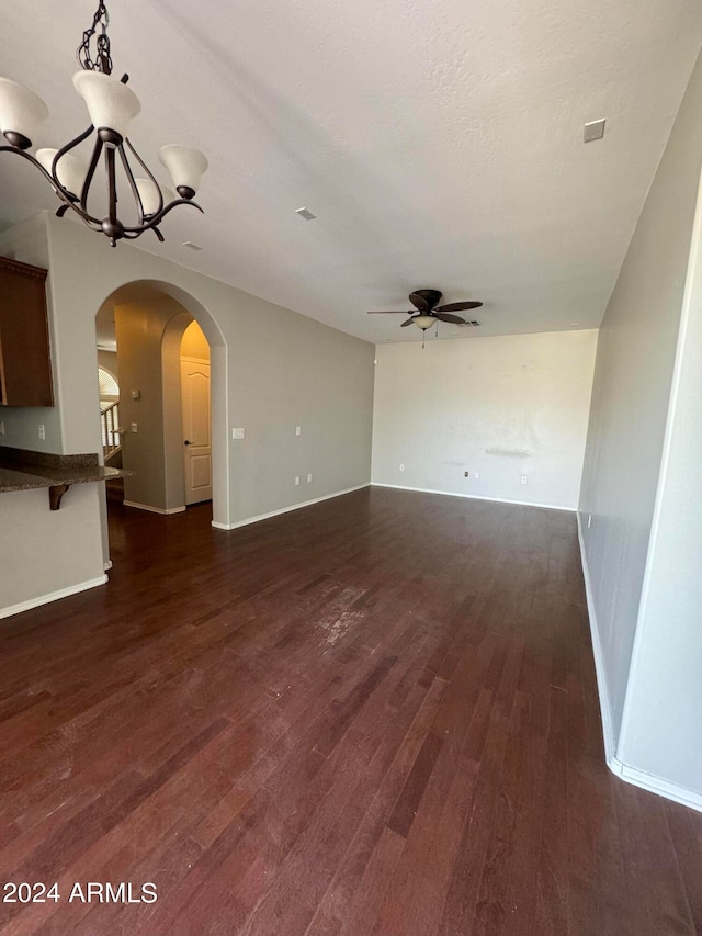 unfurnished living room featuring ceiling fan with notable chandelier and dark wood-type flooring