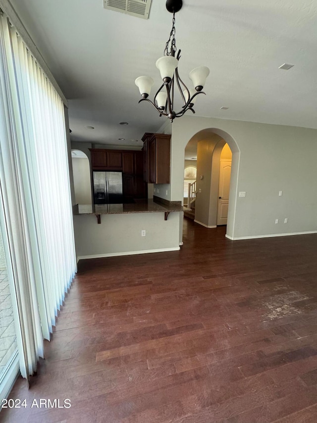 interior space with a chandelier, dark wood-type flooring, stainless steel fridge with ice dispenser, kitchen peninsula, and a kitchen breakfast bar