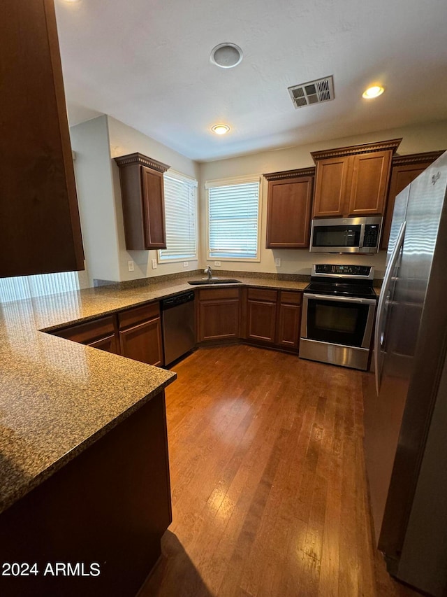 kitchen with light stone counters, dark wood-type flooring, sink, kitchen peninsula, and appliances with stainless steel finishes