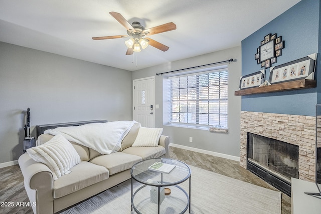 living room featuring ceiling fan, wood-type flooring, and a stone fireplace