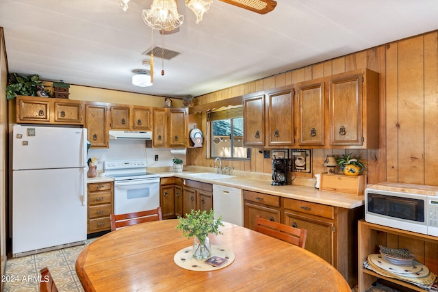 kitchen with wooden walls, white appliances, an inviting chandelier, sink, and light tile patterned flooring