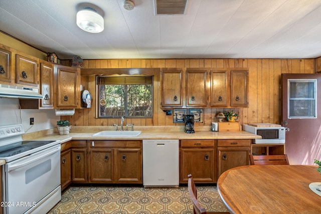 kitchen with tile patterned floors, sink, white appliances, and wooden walls