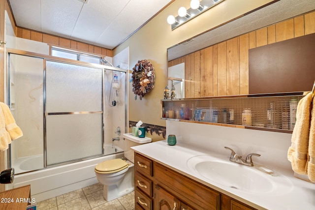 full bath featuring wooden walls, toilet, combined bath / shower with glass door, a textured ceiling, and vanity