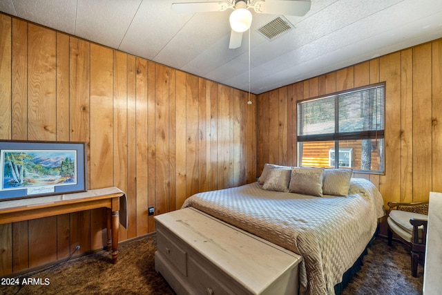 bedroom featuring wood walls, dark colored carpet, and ceiling fan