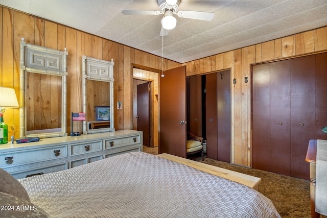 carpeted bedroom with ceiling fan, wood walls, and multiple closets