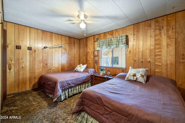 bedroom with ceiling fan, wood walls, and dark colored carpet