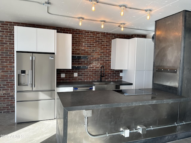 kitchen with high end refrigerator, dark countertops, brick wall, black electric stovetop, and a sink