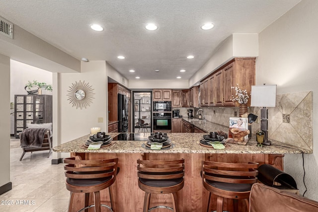 10826 E Navajo Dr, Sun Lakes, AZ 85248 - kitchen with light stone countertops, black appliances, backsplash, a sink, and a peninsula
