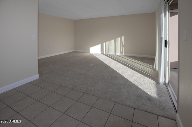 carpeted spare room featuring tile patterned flooring and baseboards