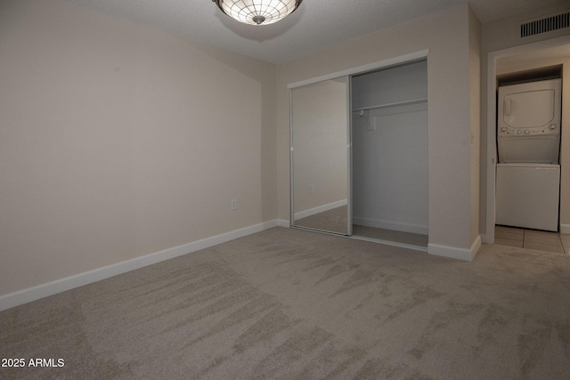 unfurnished bedroom with a closet, visible vents, stacked washer / drying machine, and carpet floors