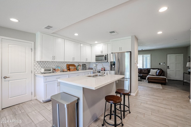 kitchen with stainless steel appliances, a center island with sink, and white cabinets