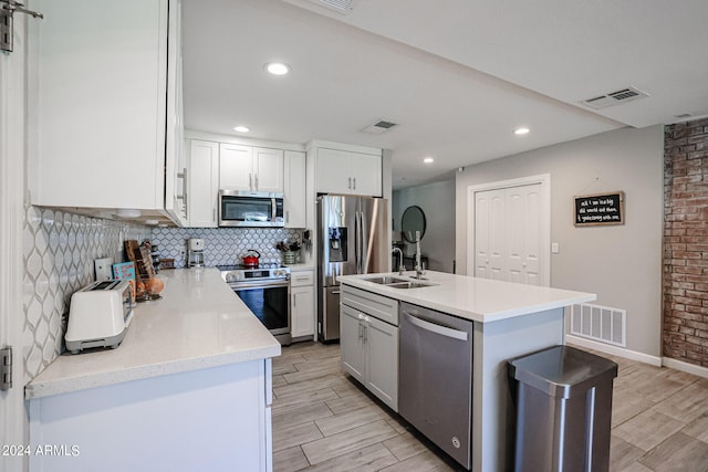 kitchen with white cabinets, decorative backsplash, sink, appliances with stainless steel finishes, and a kitchen island with sink