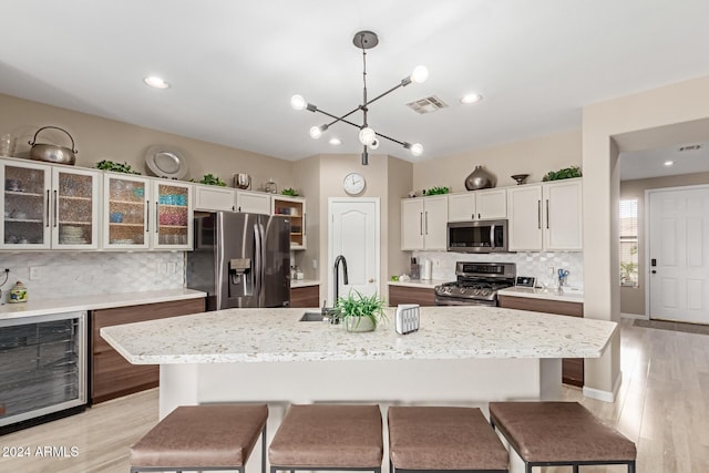 kitchen with backsplash, stainless steel appliances, pendant lighting, wine cooler, and an island with sink