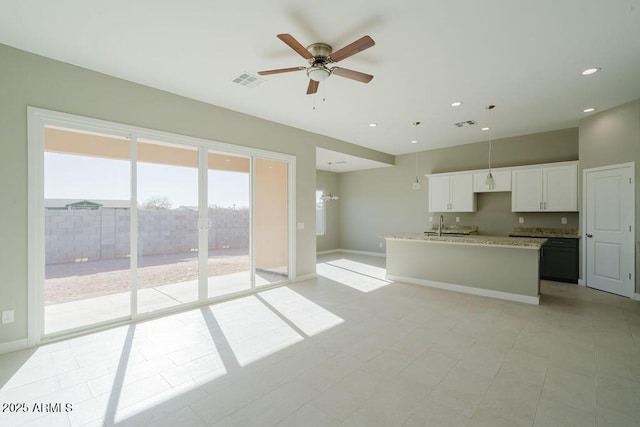 kitchen featuring light stone countertops, white cabinetry, ceiling fan, light tile patterned floors, and a center island with sink