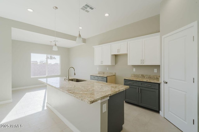 kitchen with sink, hanging light fixtures, white cabinets, and a kitchen island with sink