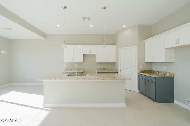 kitchen featuring decorative light fixtures, white cabinets, and an island with sink