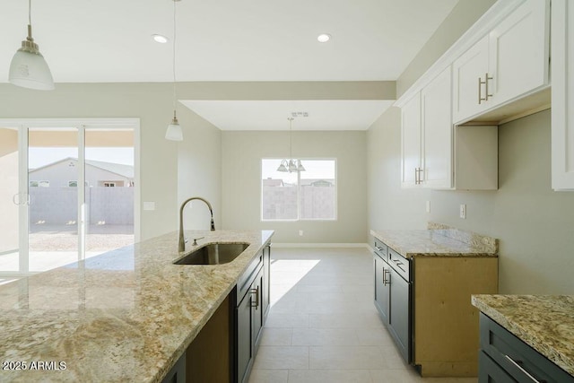 kitchen with decorative light fixtures, sink, light stone counters, and white cabinetry