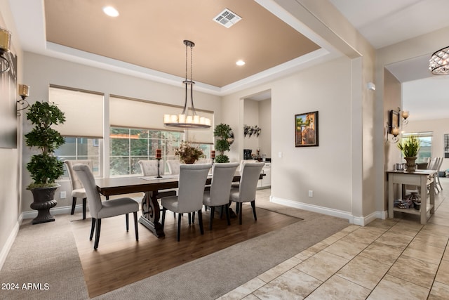 dining area featuring an inviting chandelier, a healthy amount of sunlight, a tray ceiling, and light hardwood / wood-style flooring