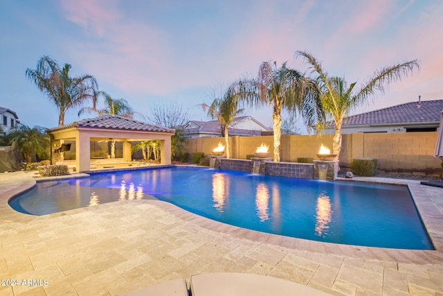 pool at dusk with pool water feature, an outdoor kitchen, and a patio area