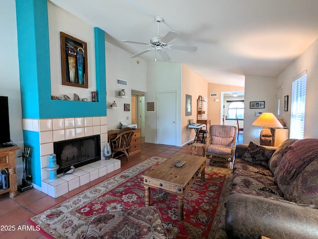 living room featuring tile patterned flooring, visible vents, a tiled fireplace, vaulted ceiling, and a ceiling fan