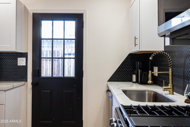 kitchen featuring stainless steel microwave, light stone countertops, white cabinetry, backsplash, and gas stove