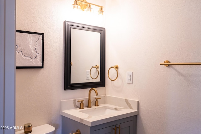 half bath featuring toilet, a textured wall, and vanity