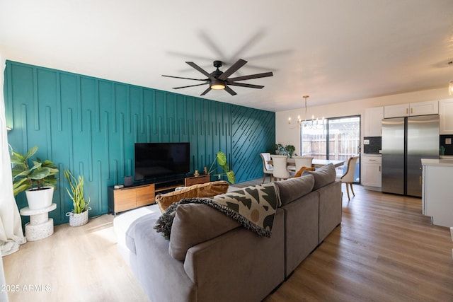 living room with an accent wall, wood finished floors, and ceiling fan with notable chandelier