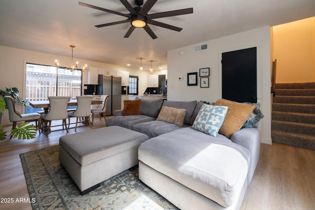 living room with ceiling fan with notable chandelier, wood finished floors, visible vents, and stairs