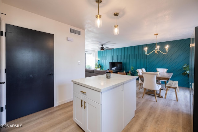 kitchen with a kitchen island, visible vents, white cabinets, light wood-style floors, and decorative light fixtures