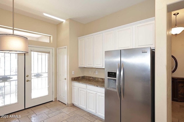 kitchen with stone tile floors, stainless steel fridge with ice dispenser, stone countertops, white cabinets, and pendant lighting