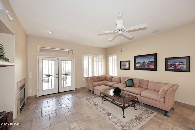 living room featuring a ceiling fan, stone tile floors, french doors, and baseboards